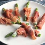 prosciutto wrapped asparagus served on a white plate
