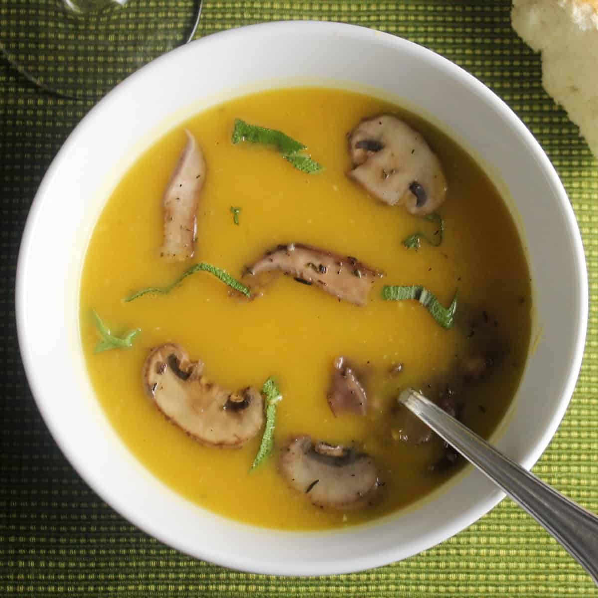 creamy butternut squash soup topped with mushrooms and sage, served in a white bowl.