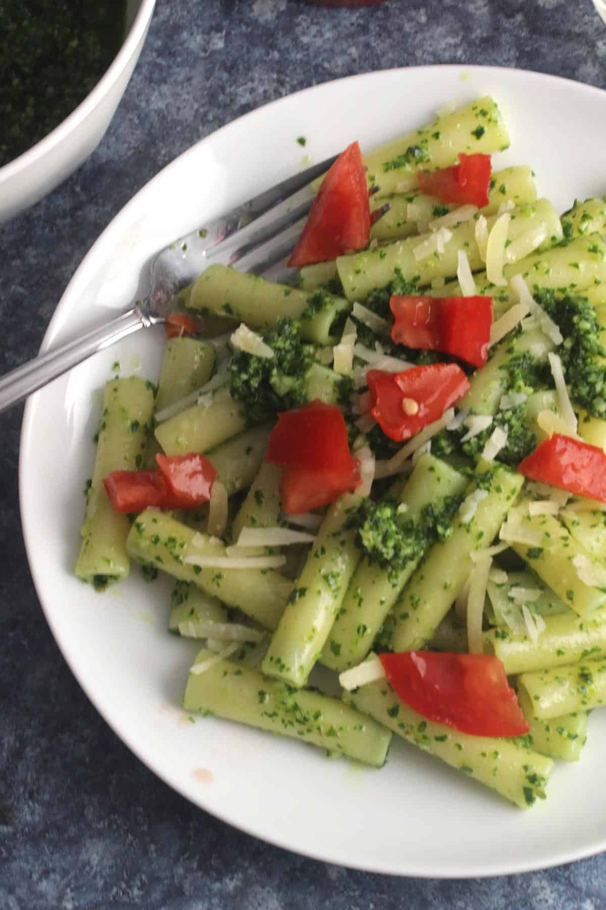 kale pesto pasta plated topped with tomatoes