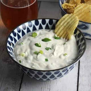 bowl of green onion dip next to a bowl of chips and a beer.