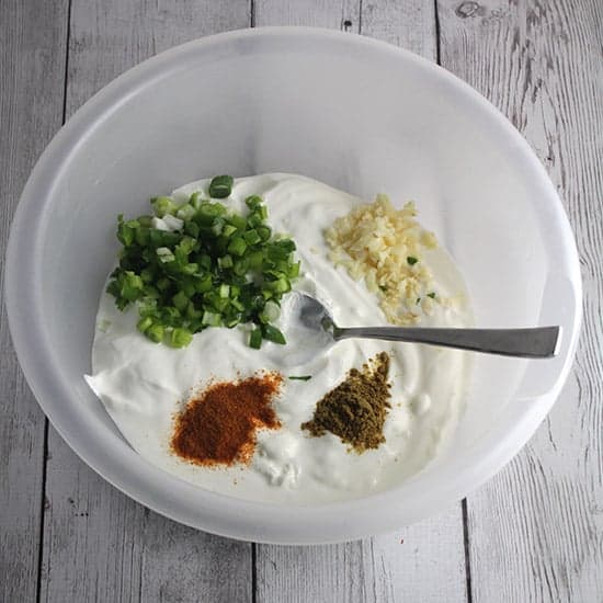 green onions, garlic and spices in a bowl with sour cream.