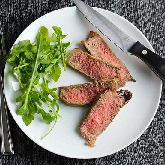 slices of NY strip steak plated with arugula.