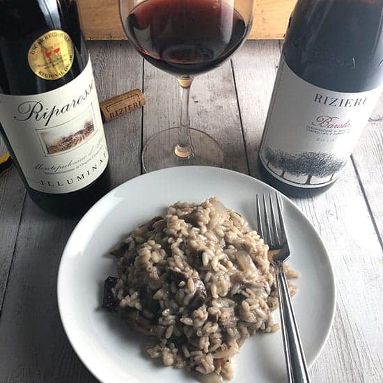 mushroom risotto on a plate with two bottles of Italian red wine.