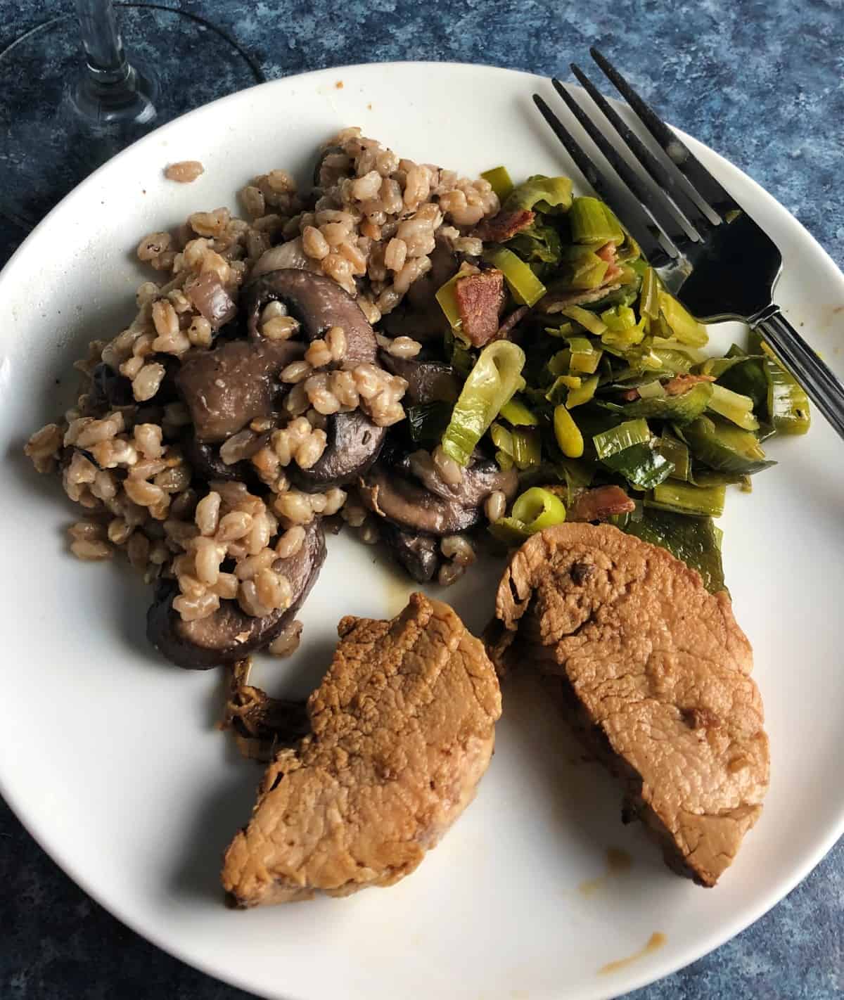 white plate with pork tenderloin and leek greens.