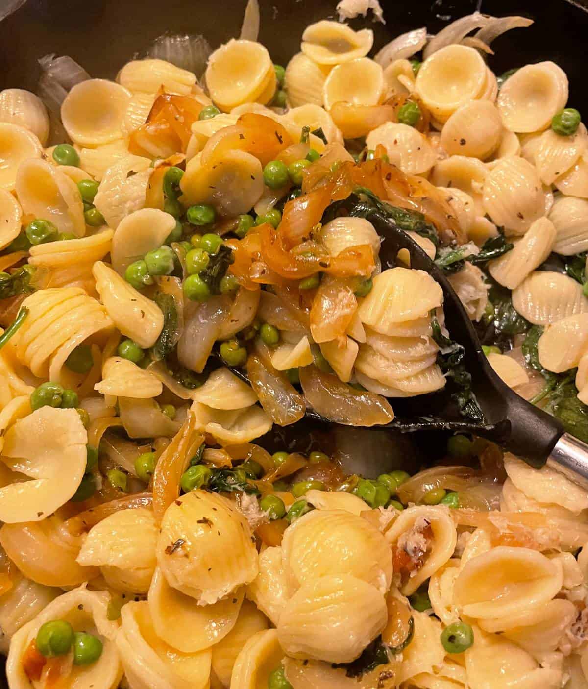 stirring orecchiette pasta into a skillet with peas and onions.