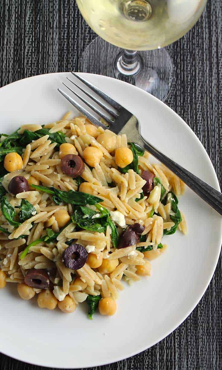 Greek orzo with spinach, olives and feta on a white plate.