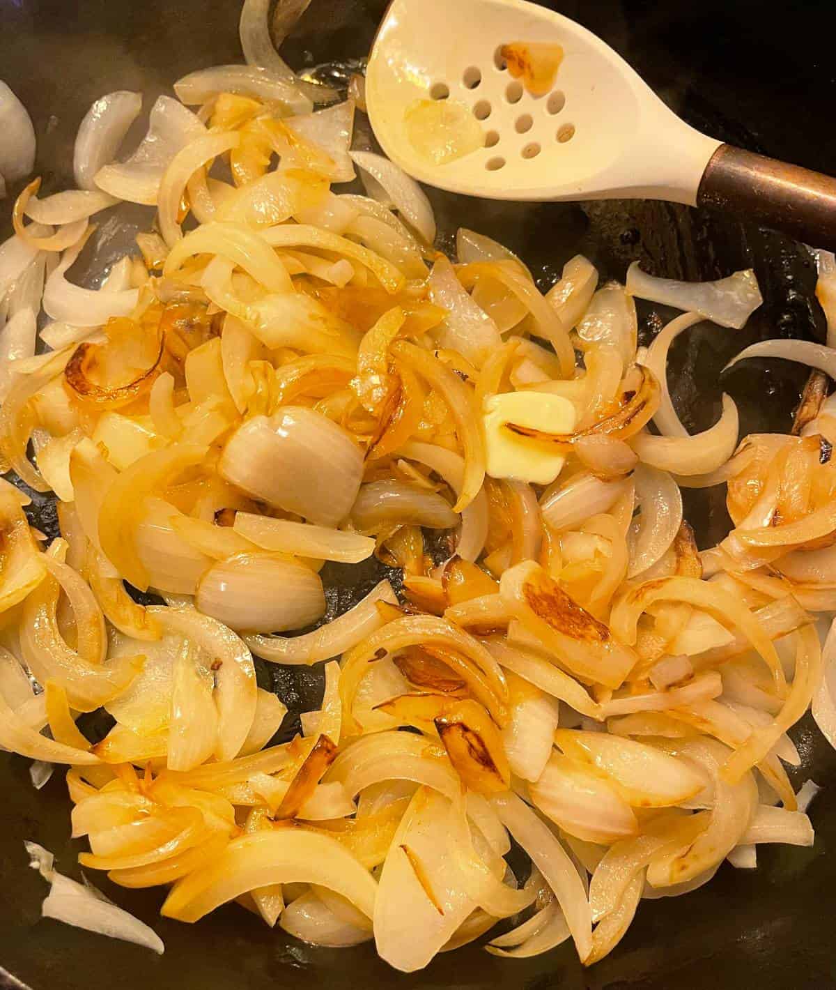 adding butter to caramelized onions in a skillet.