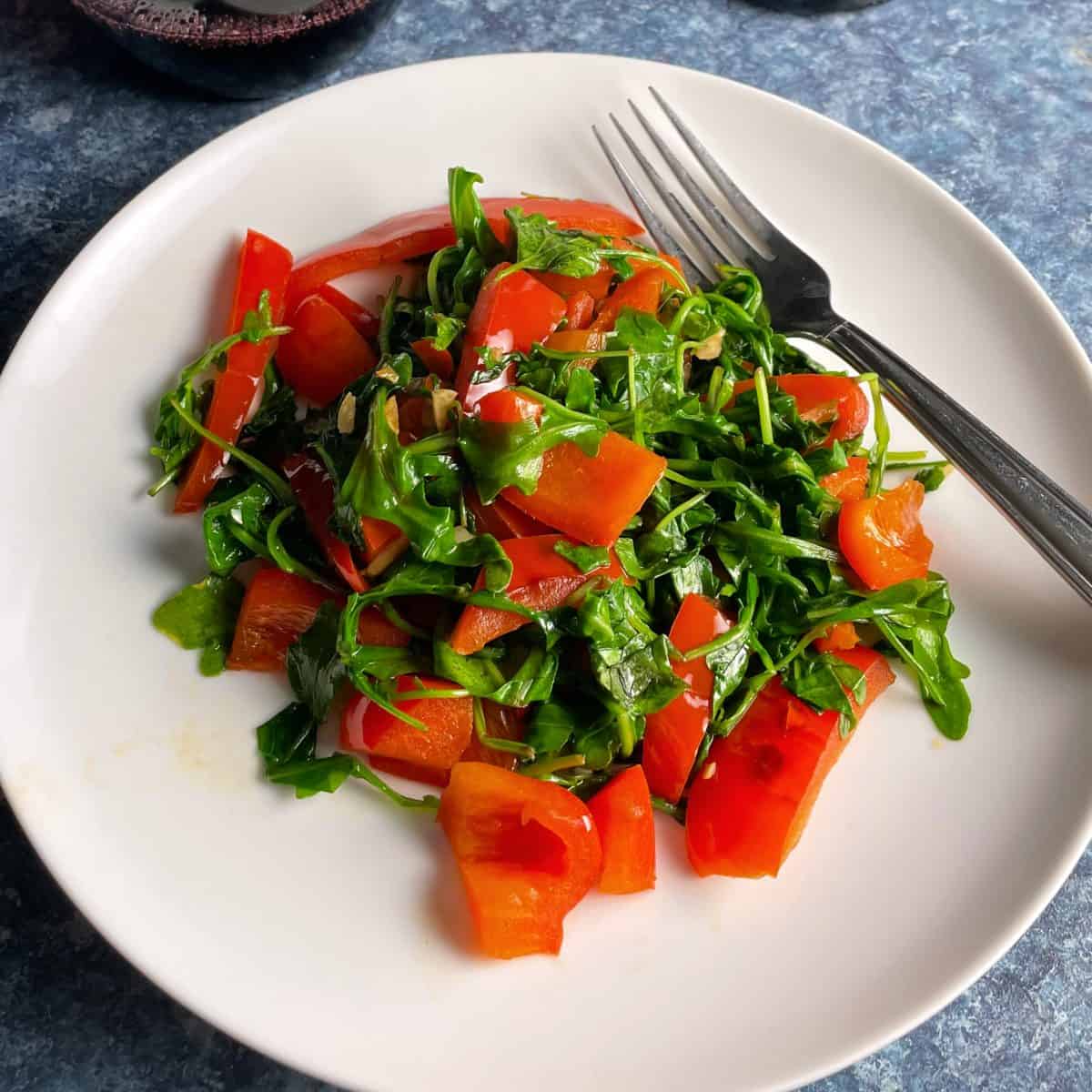 sautéed arugula and red bell peppers served on a white plate.