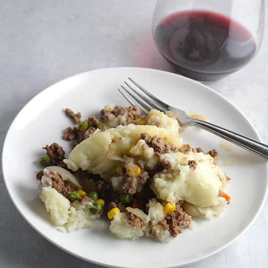 beef shepherd's pie casserole served on a white plate with a glass of red wine.