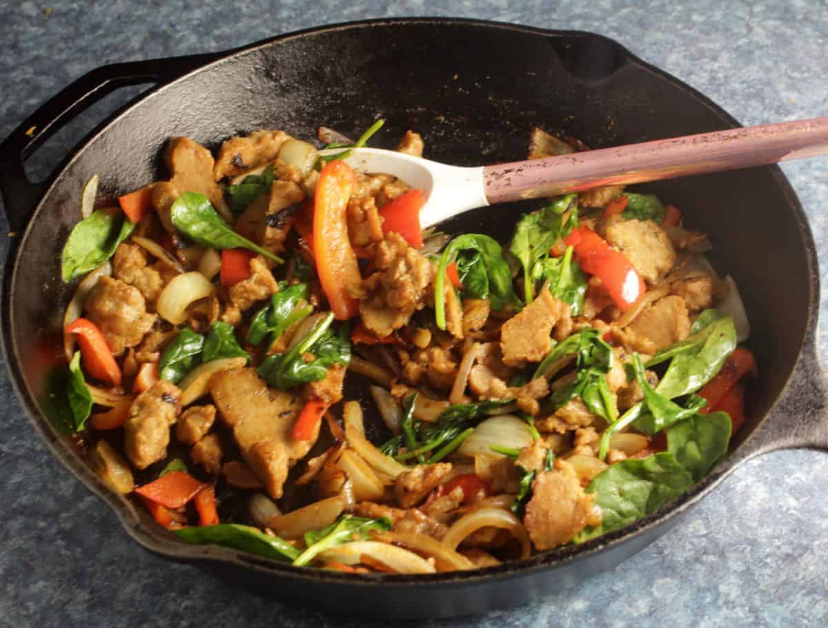 seitan with peppers and onions in a black skillet.