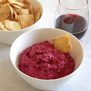 roasted beet dip in a bowl with a glass of red wine beside it.
