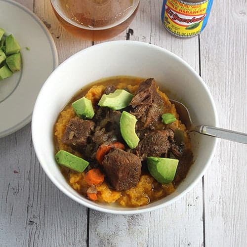 bowl of spicy beef stew with avocado slices on top.