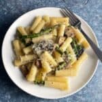 asparagus and mushroom pasta on a white plate topped with grated Parmesan cheese.