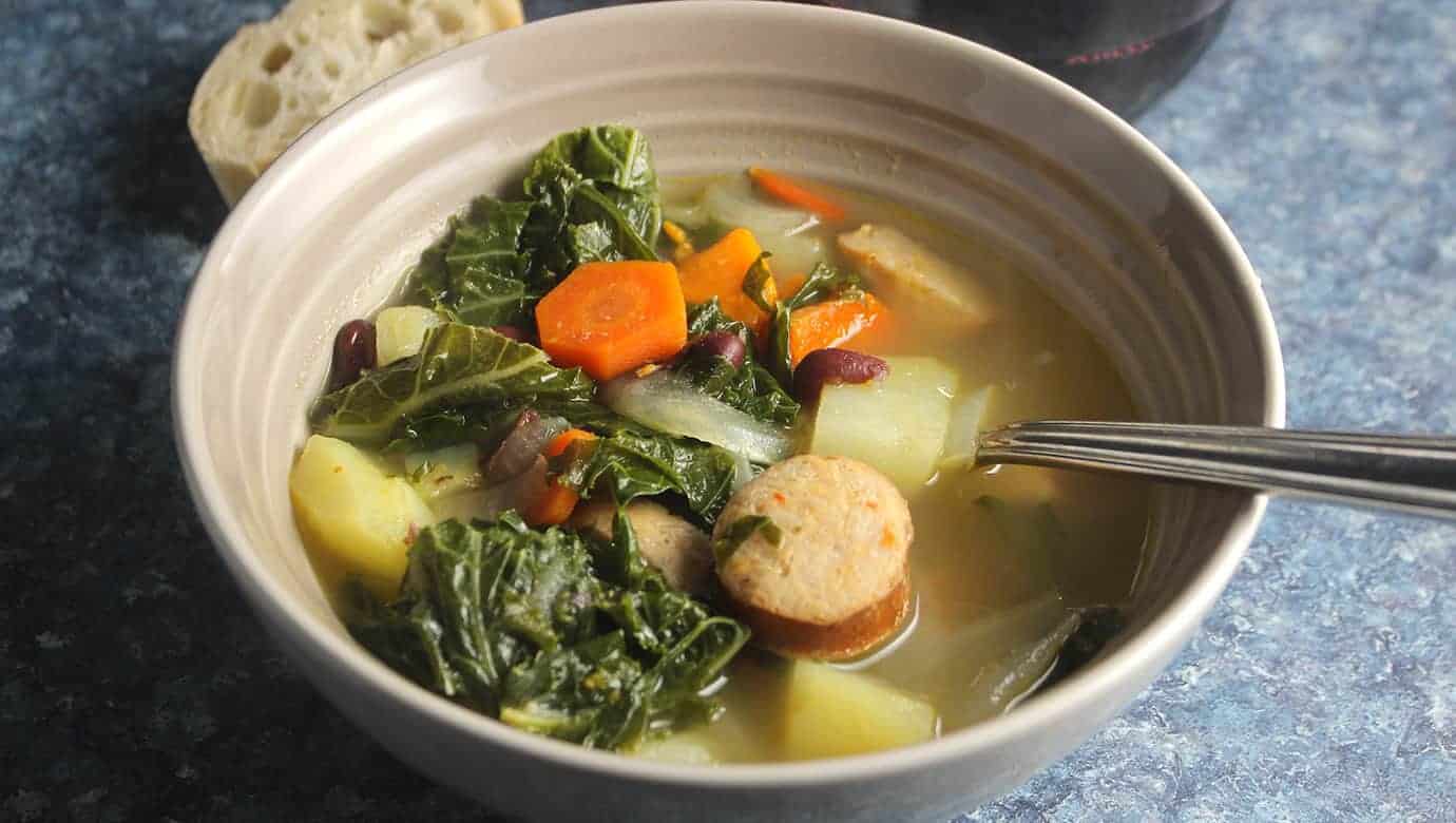 portuguese kale soup in bowol, with sausage, carrots and kale near the top.
