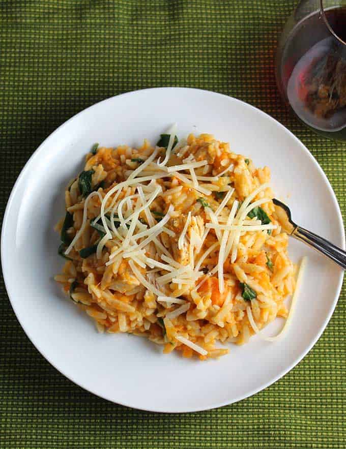 Orzo with leftover turkey and sweet potatoes on a white plate, served with a glass of red wine. 