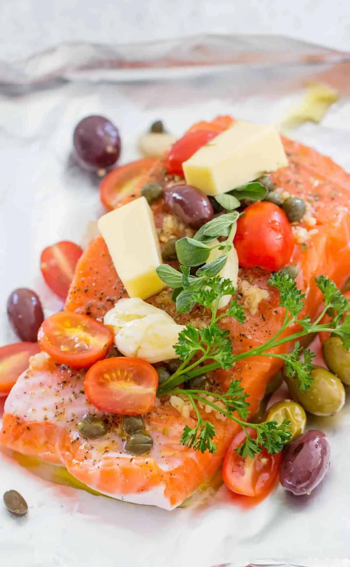 a cooked salmon fillet topped with tomatoes, olives and herbs.