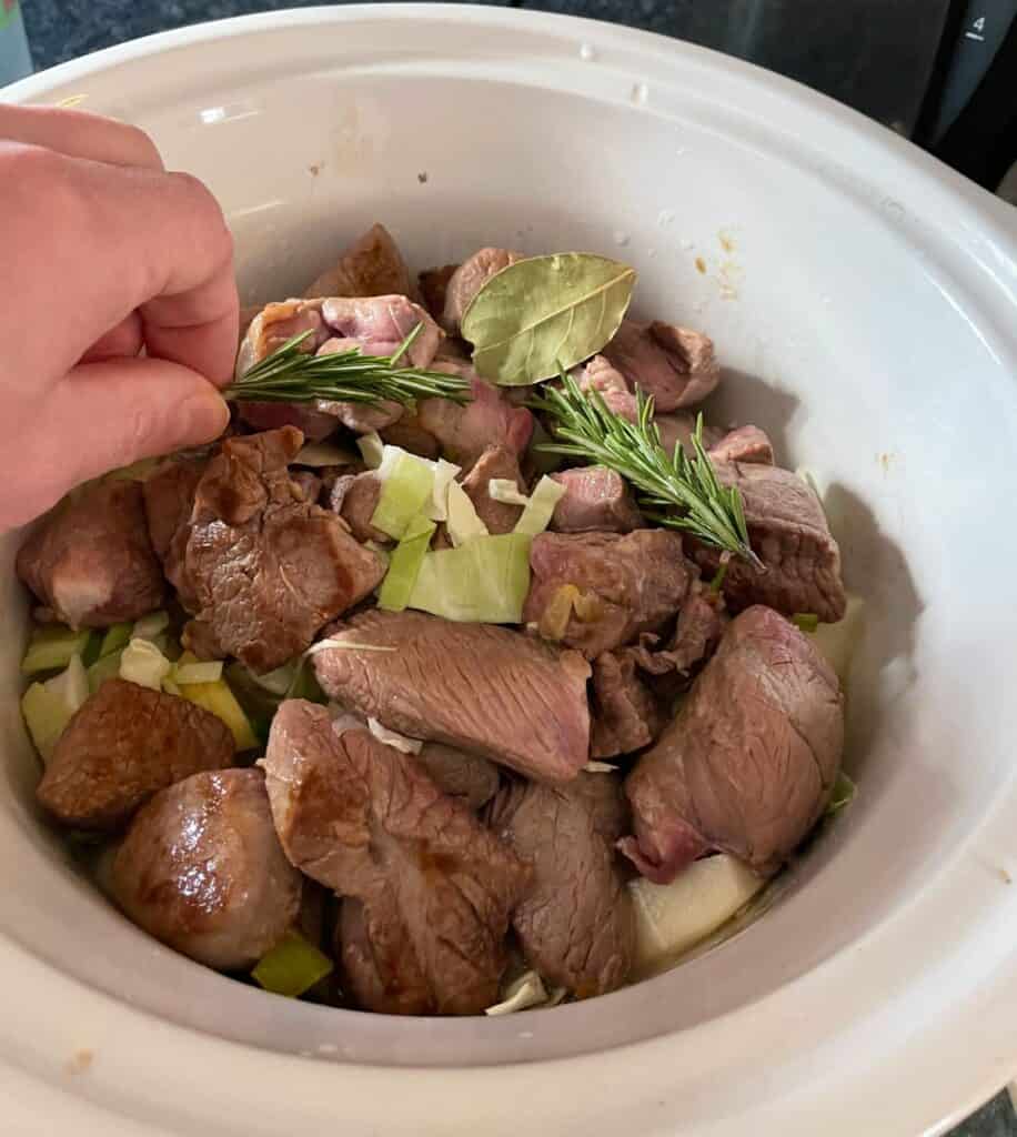 adding herbs along with lamb in a slow cooker.