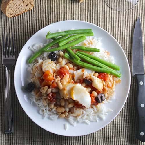 cod and beans served on a plate over rice, with a side of green beans.