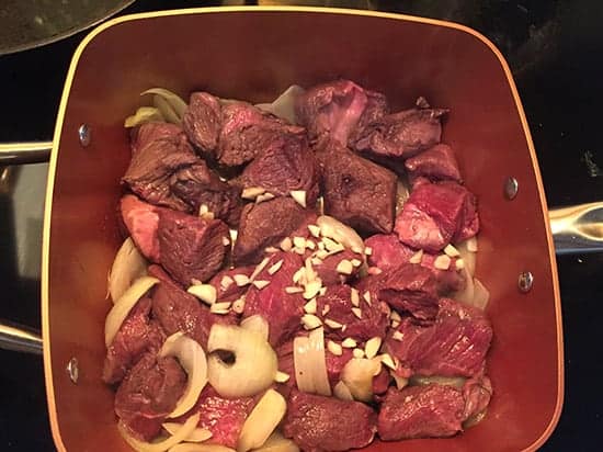 stew beef in a copper pan with onions.