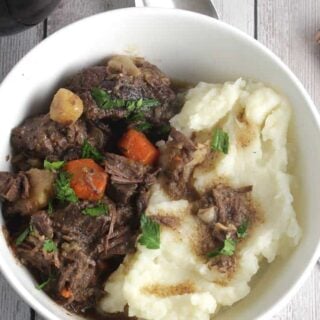 bowl of beef stew with mashed potatoes on the side.