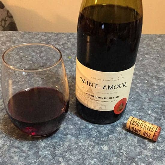 open bottle of Saint-Amour Cru Du Beaujolais with a glass of the red wine beside it.