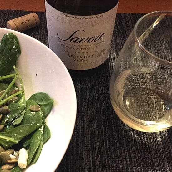 bottle of Savoie white wine with a glass on one side, spinach salad on the other side.