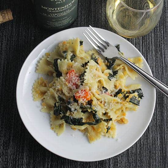 tuscan kale pasta on a plate with a glass of white wine on the side.