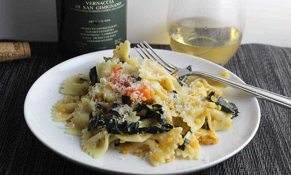 closeup of tuscan kale pasta on a plate with Vernaccia white wine in background.