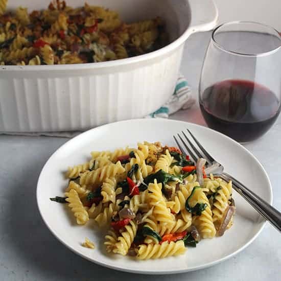 plate of vegetarian baked pasta with a glass of red wine on the side, and casserole dish in the background.