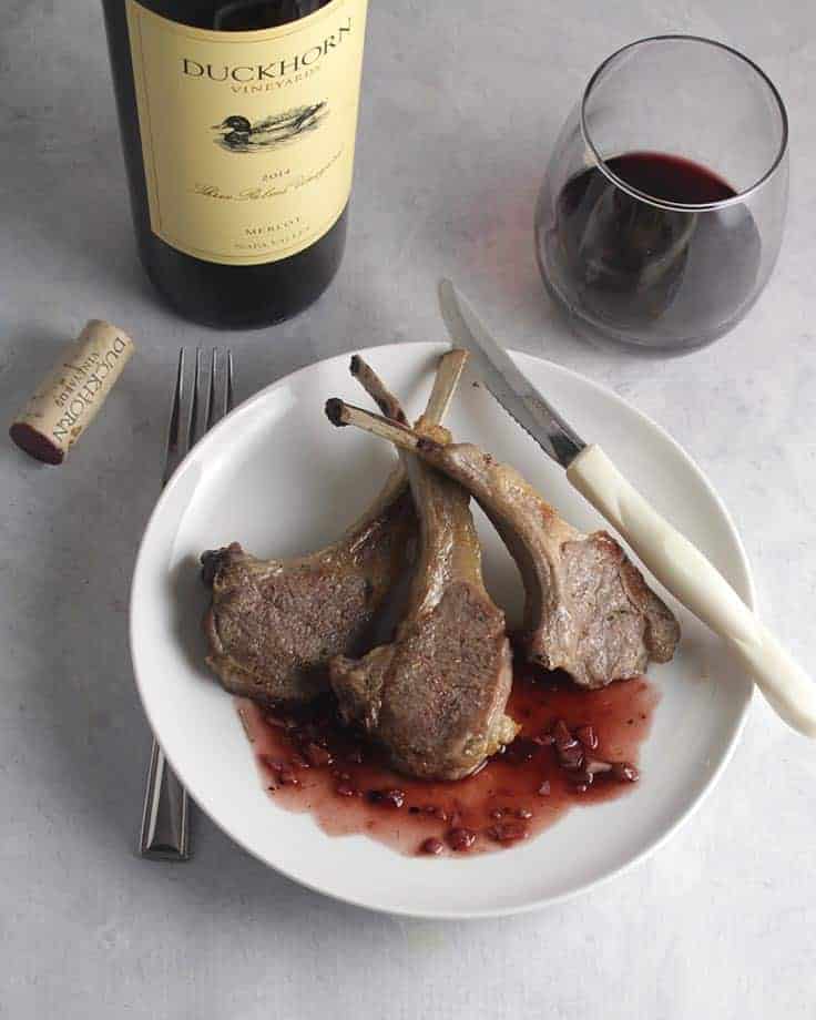 bottle of Duckhorn Merlot with roasted lamb chops on a plate with blackberry sauce.