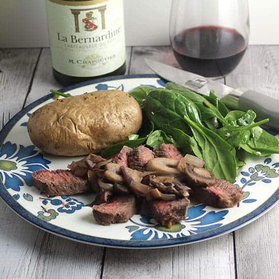 London broil steak topped with mushrooms served with potato, salad and red wine.