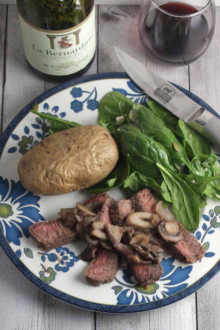 London broil steak top with mushrooms served with potatoes and salad, paired with red wine.