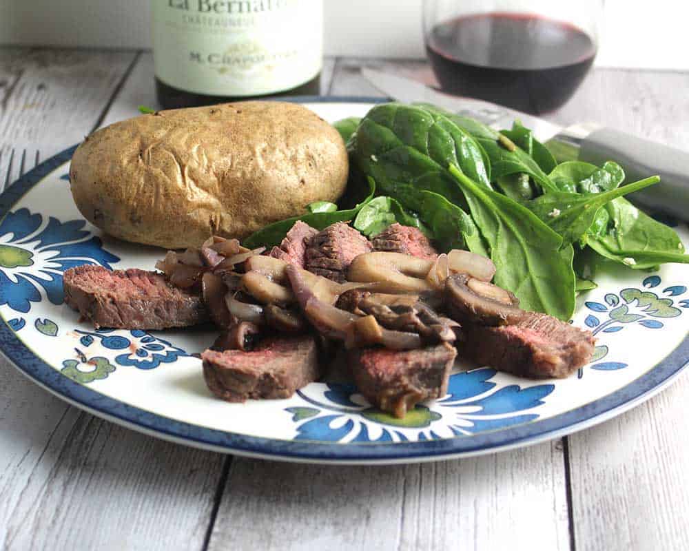 sliced London broil steak topped with mushrooms.