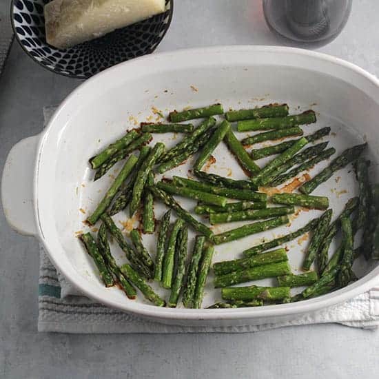 roasted asparagus with parmesan in a white baking dish.