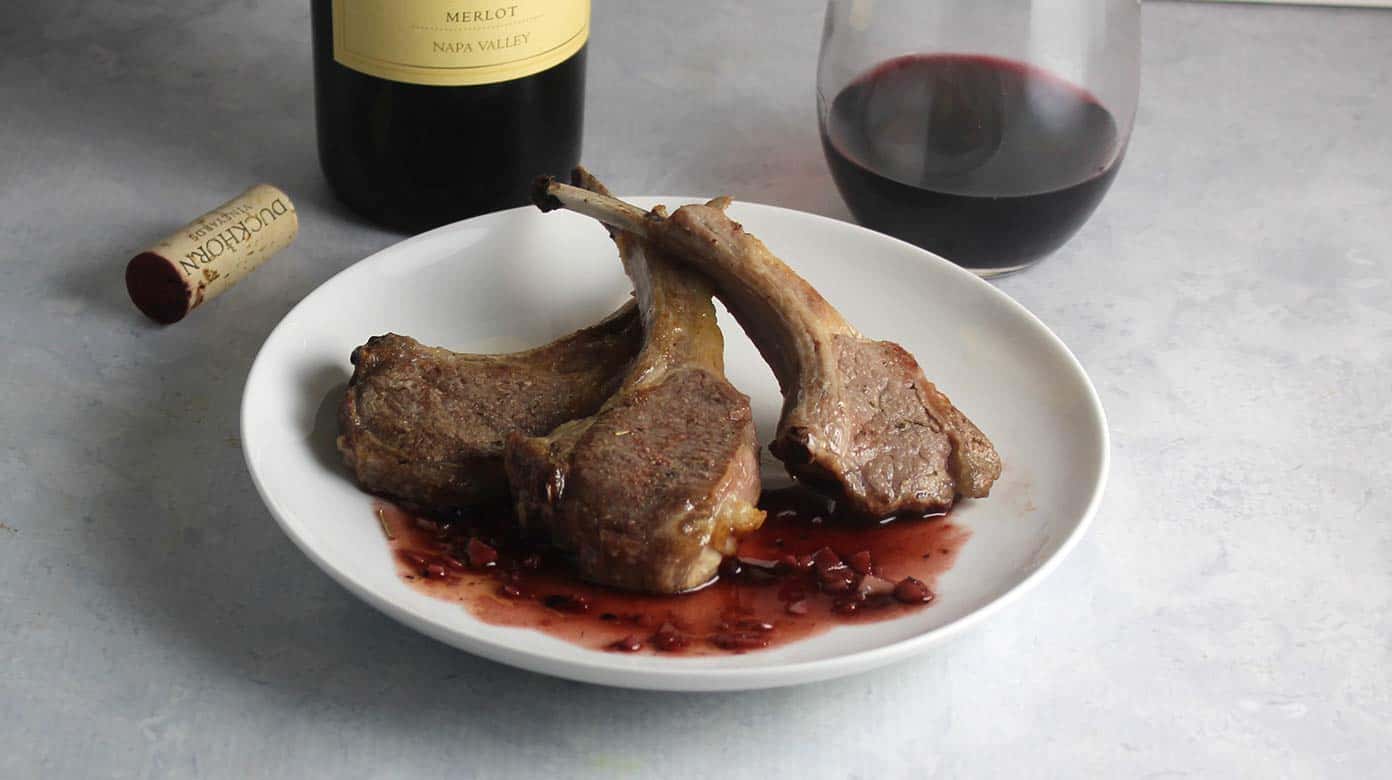 roasted lamb chops on a plate with blackberry sauce.