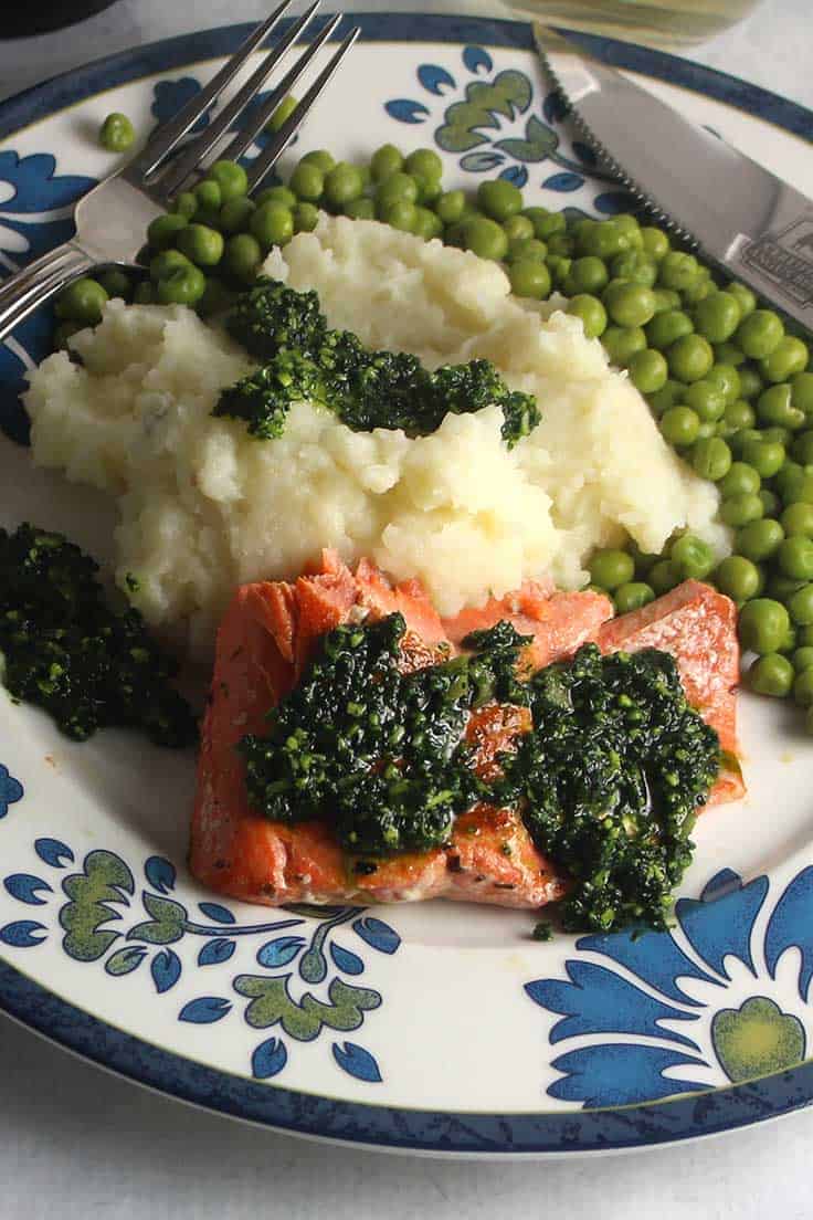 salmon topped with kale pesto on a plate with mashed potatoes and peas.