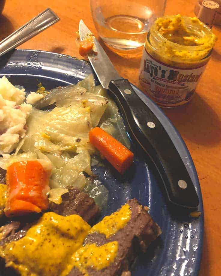 corned beef and cabbage on a plate with jar of mustard and glass of white wine nearby.