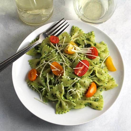 plate with bowtie pasta tossed with pesto, topped with tomatoes.