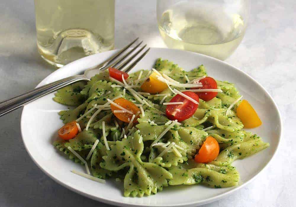bow tie pasta with pesto and tomatoes on a plate with white wine.