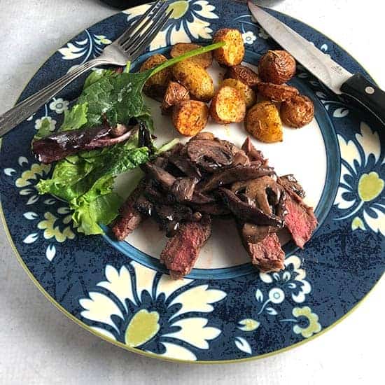 steak with Manchego mushroom sauce on a plate with potatoes and salad.