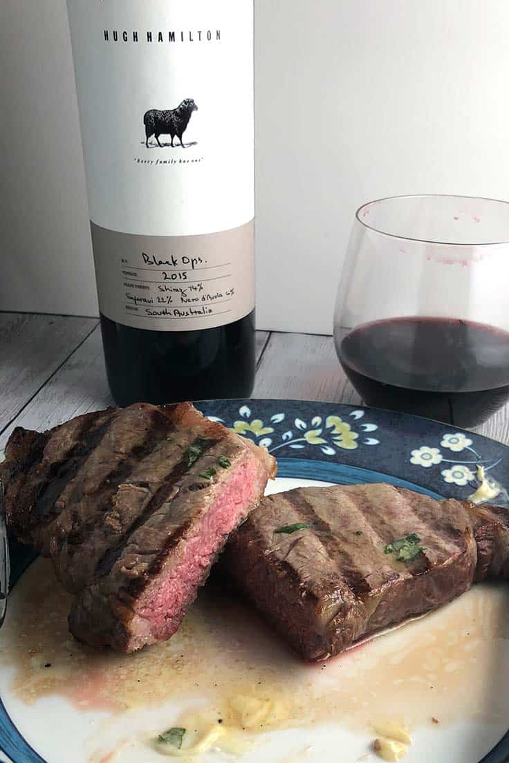 grilled steak on a plate with a bottle of Shiraz in the background.