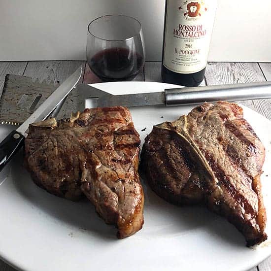 bistecca alla Fiorentina on a platter with red wine in background.