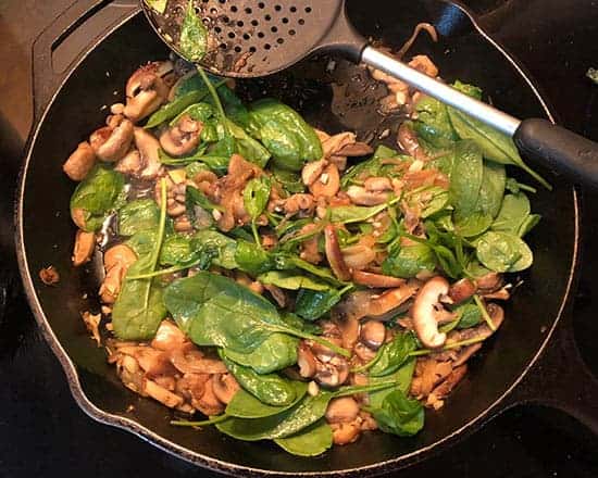 spinach and mushrooms cooking in a skillet.