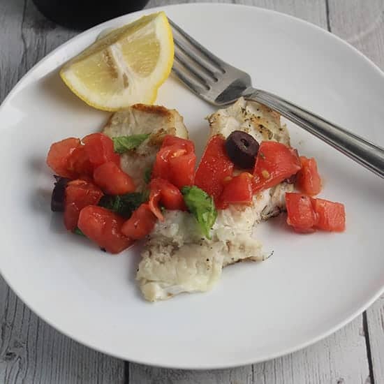 grilled tilapia with tomatoes on a white plate.