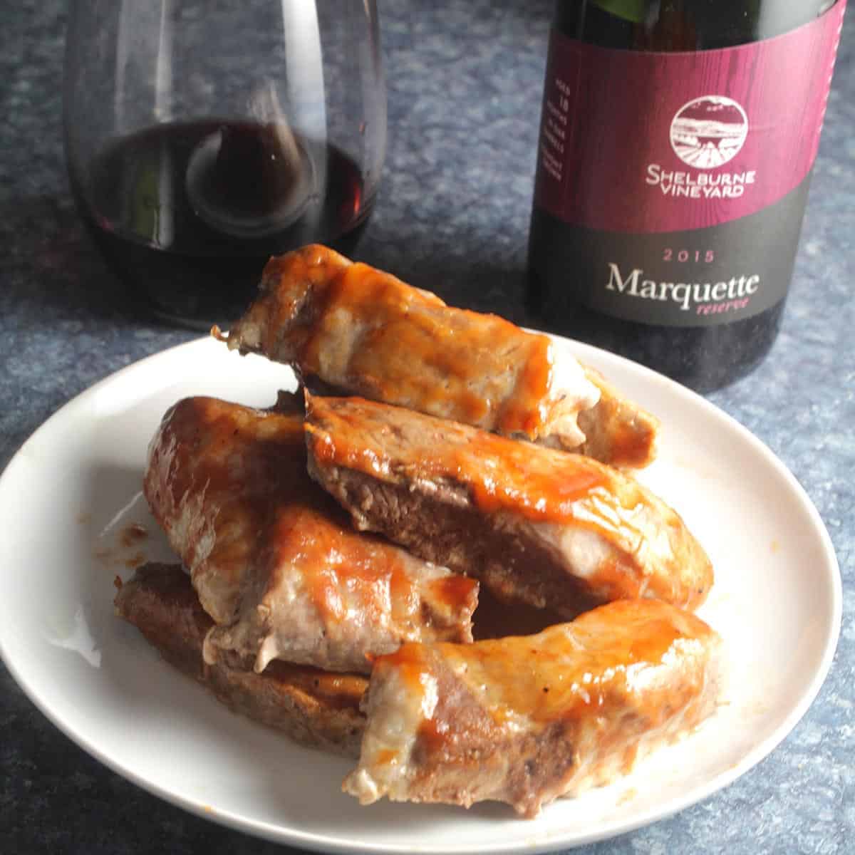 baked boneless pork ribs served on a plate with a bottle of red wine.