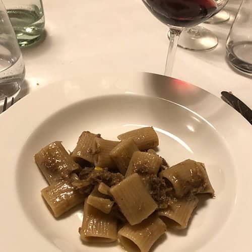 pasta with meat sauce in a white dish, with a glass of red wine.