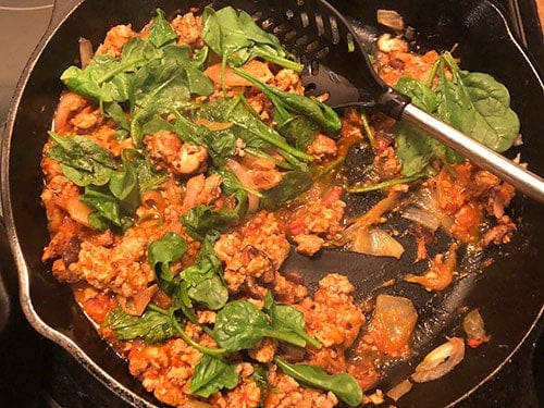 making a quick pasta sauce in the skillet with turkey, tomato sauce and spinach.