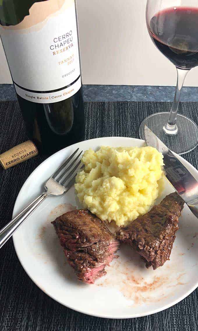 BBQ baked steak tips on a plate with mashed potatoes and red wine.