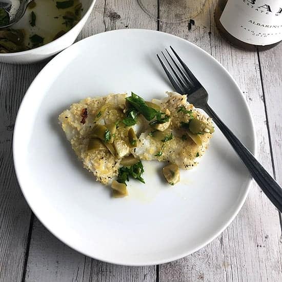 baked cod on a plate topped with olive relish.