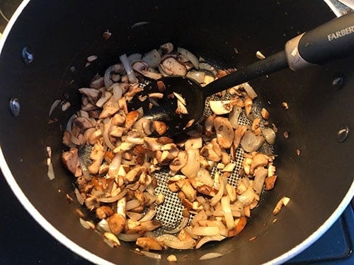sautéing mushrooms and onions in a pot.